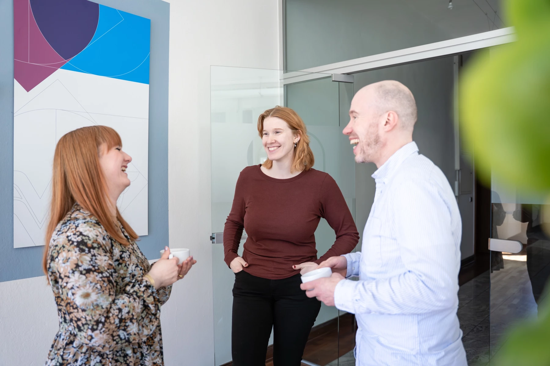 Sina Kunz (Projektmanagement) und zwei Teammitglieder lachen gemeinsam bei einem Kaffee im Büro in Lüneburg